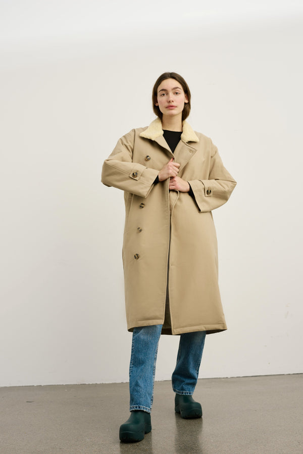A model wears a beige MEOTINE coat with a soft collar, paired with blue jeans and green shoes, set against a neutral background.
