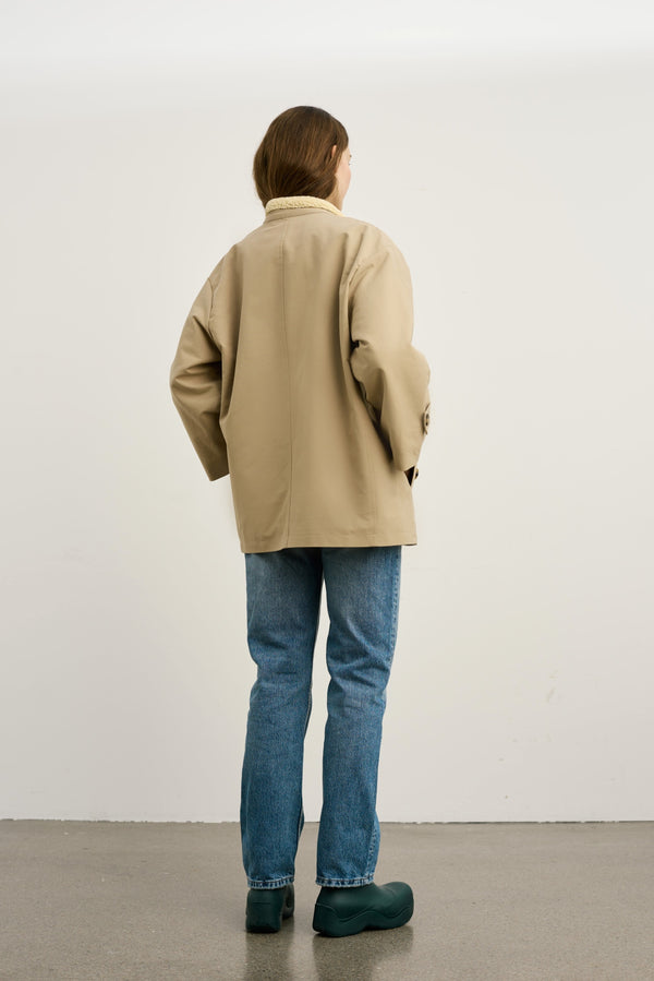 A woman in a beige oversized jacket and blue jeans stands with her back to the camera, showcasing a casual MEOTINE style.