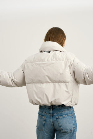 A model showcases a stylish MEOTINE puffer jacket from the back, featuring a cropped design and relaxed fit, paired with jeans.