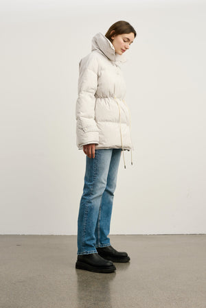 A model wearing a light beige MEOTINE puffer jacket with a cinched waist, paired with blue jeans and black platform boots.