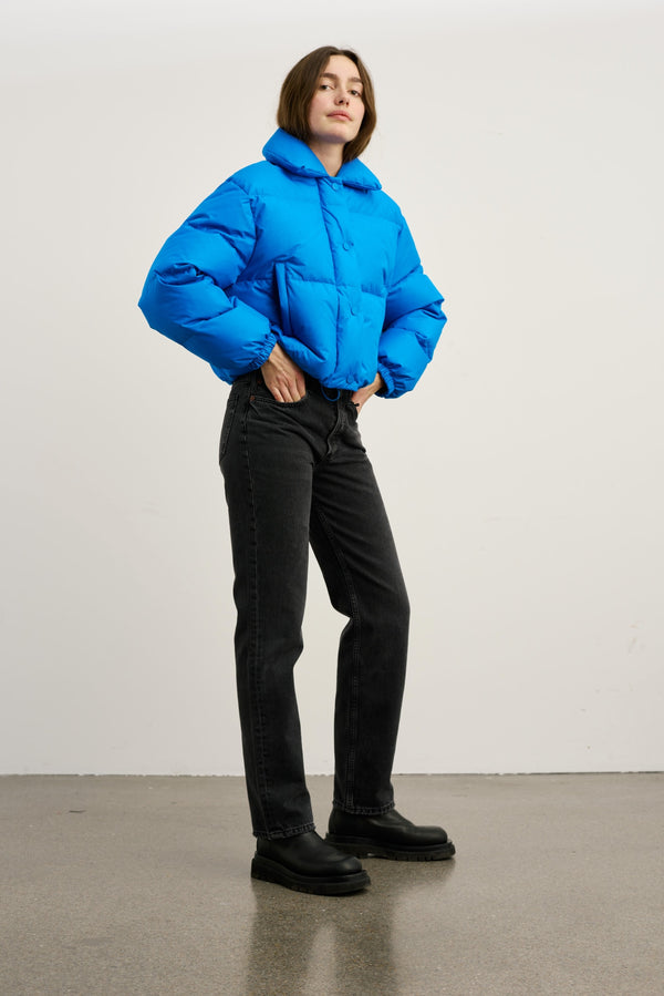 A model showcases a vibrant blue puffer jacket paired with black jeans and chunky boots, embodying MEOTINE's stylish winter look.