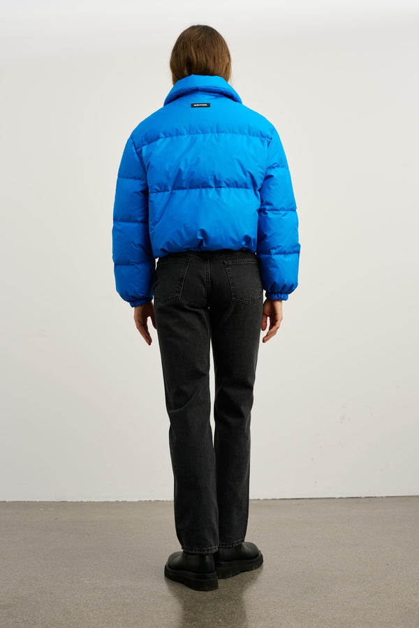 A person wearing a vibrant blue puffer jacket from MEOTINE, paired with black jeans, stands against a neutral background.