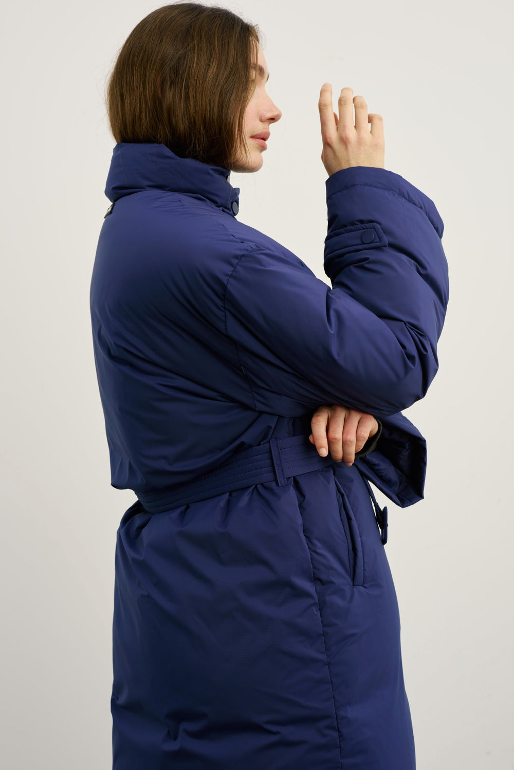 A model showcases a long navy blue puffer coat with a high collar and front pockets, paired with relaxed denim jeans and sneakers. MEOTINE.
