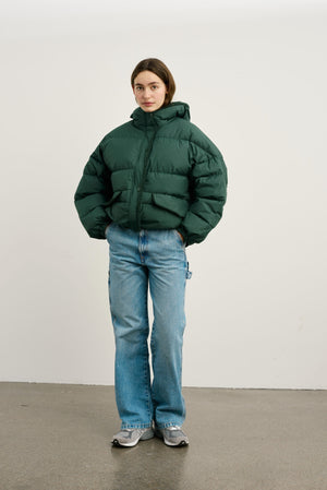 A model wears a green puffer jacket paired with light blue flared jeans, showcasing MEOTINE's stylish winter outerwear.