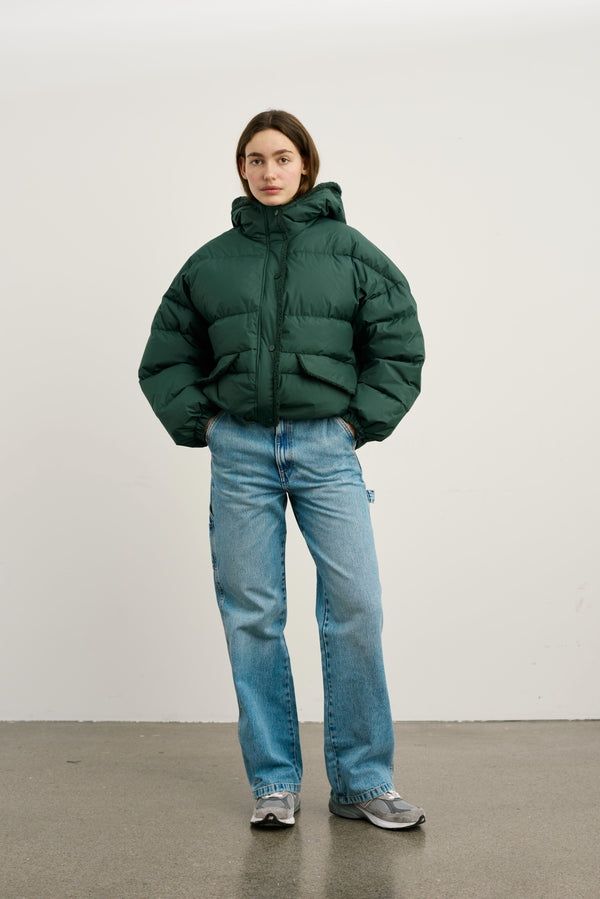 A model wears a green puffer jacket with a hood, paired with light blue jeans and sneakers, showcasing MEOTINE's stylish outerwear.