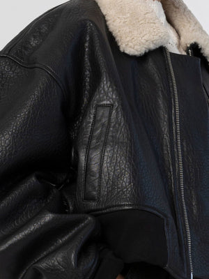 A close-up of a black leather jacket with a cozy shearling collar, showcasing its textured finish and stylish design by MEOTINE.