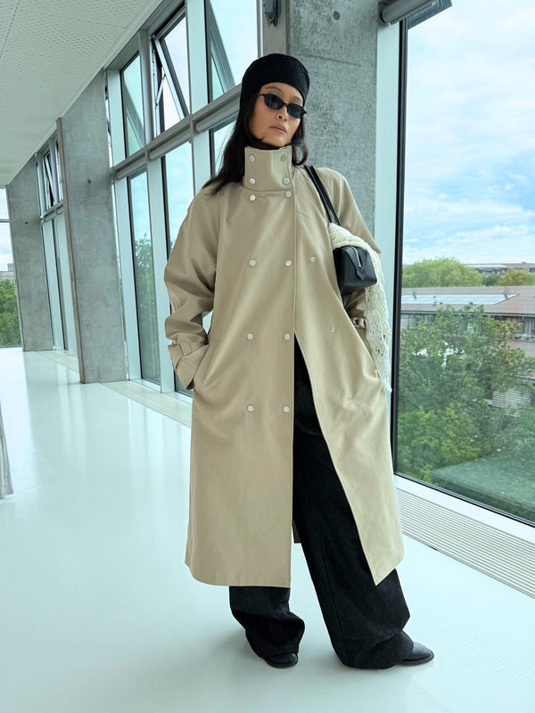 A model showcases a stylish beige trench coat with a relaxed fit, paired with black wide-leg pants and accessories, embodying MEOTINE's chic aesthetic.