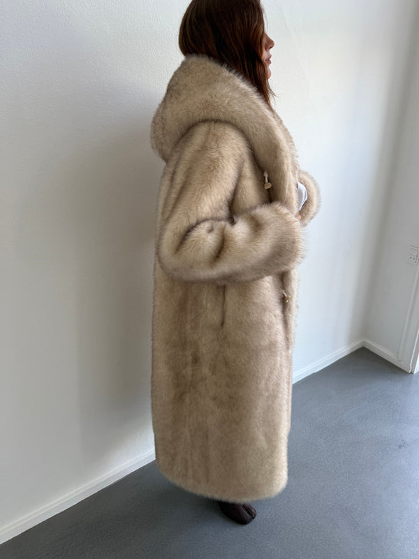 A model showcases a luxurious beige MEOTINE coat with a plush hood, highlighting its elegant and cozy design from the side.
