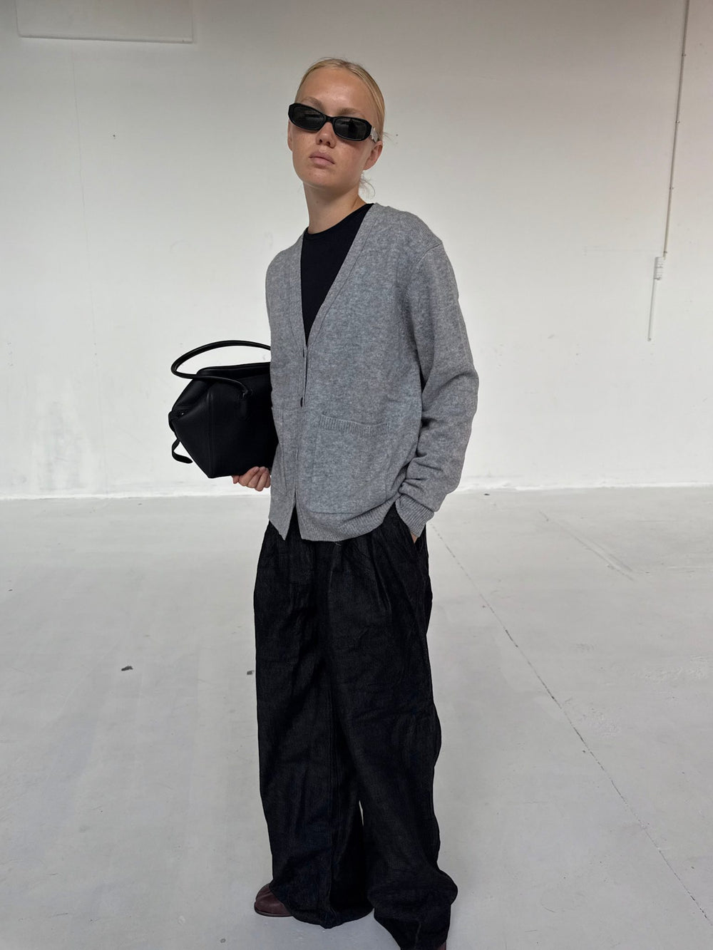 A model wearing a gray cardigan over a black top, holding a black bag, showcasing MEOTINE's stylish and modern aesthetic.
