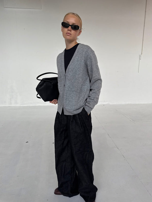 A model showcases a stylish gray cardigan paired with wide black trousers, exuding a chic vibe, complemented by a sleek bag. MEOTINE.