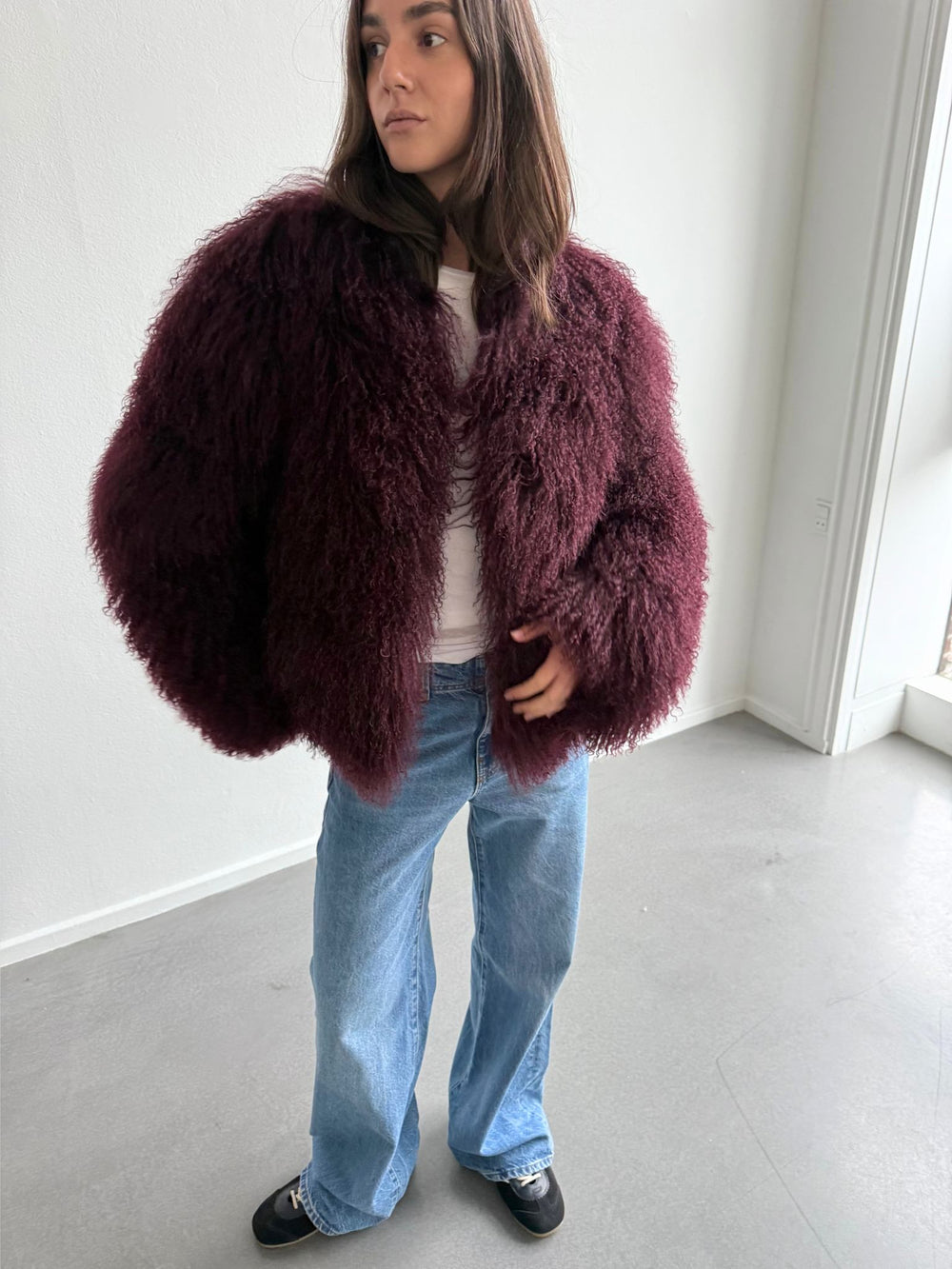 A model showcases a plush, burgundy MEOTINE jacket paired with light blue flared jeans, exuding a cozy, stylish vibe.