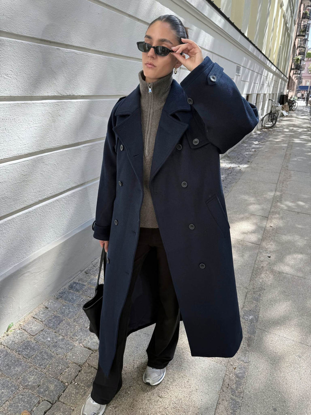 A model wears a stylish navy trench coat with a belt, paired with black pants and sunglasses, showcasing MEOTINE's chic design.