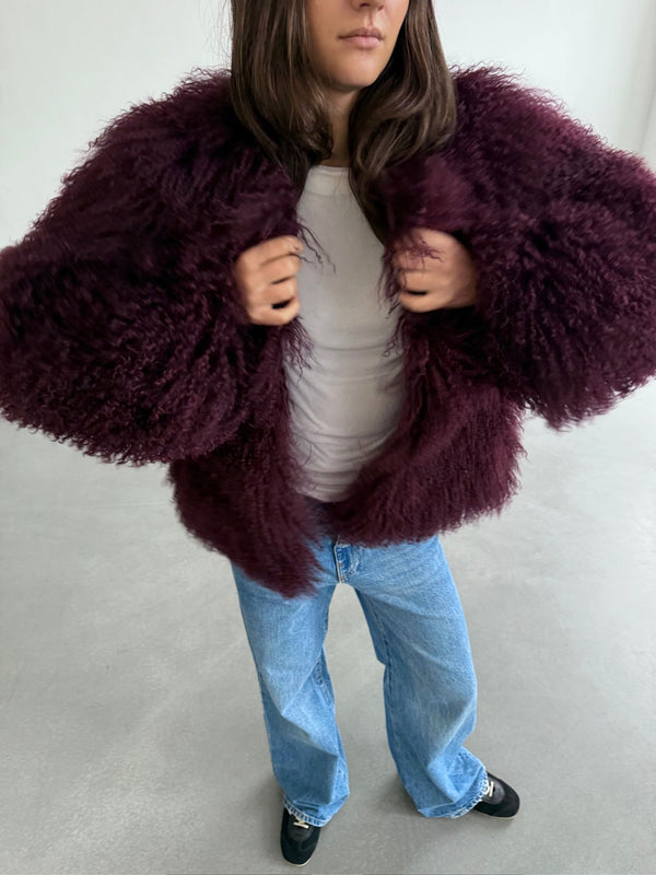 A model wears a fluffy, burgundy MEOTINE jacket over a white top, paired with light blue jeans and black shoes.