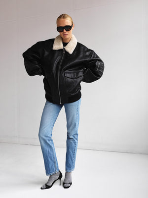 A model showcases a stylish black leather jacket with a fur collar, paired with blue jeans and sleek heels, embodying MEOTINE's chic aesthetic.
