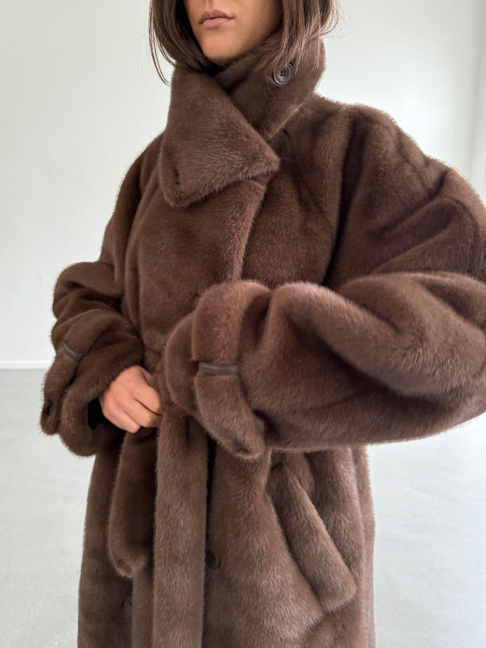 Cozy brown faux fur coat with a belted waist, featuring a high collar, worn over casual jeans and black shoes. MEOTINE.