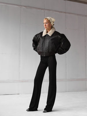 A model showcases a stylish black leather jacket with a fur collar, paired with sleek black pants, embodying MEOTINE's chic aesthetic.