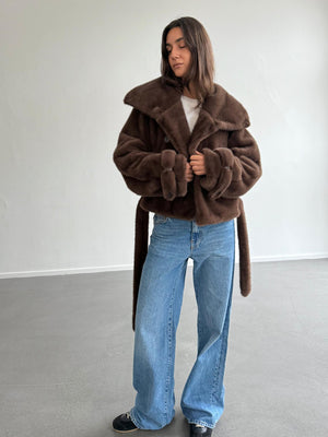 A model wears a cozy brown faux fur jacket from MEOTINE, paired with wide-leg jeans, showcasing a stylish and relaxed look.