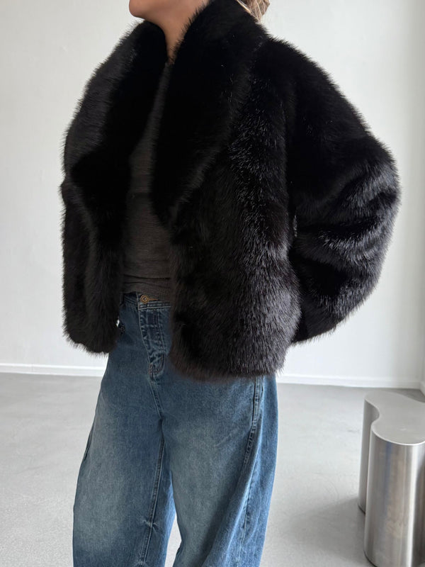 A model showcases a stylish black fur jacket by MEOTINE, paired with relaxed denim jeans, set against a minimalist background.