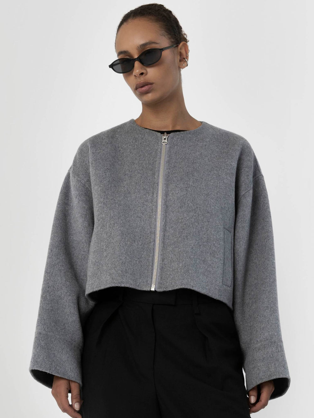 A model wears a cropped gray jacket with a zip front and wide sleeves, paired with black trousers and stylish sunglasses. MEOTINE.