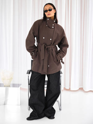 A model showcases a stylish brown MEOTINE jacket with a belted waist, paired with wide-leg dark jeans and sunglasses.