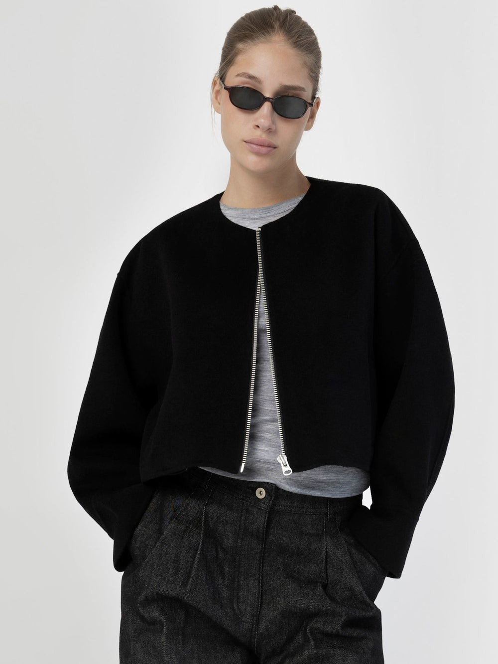 A model wearing a black cropped jacket with a zip front, paired with a gray top and stylish sunglasses, showcasing MEOTINE's modern design.