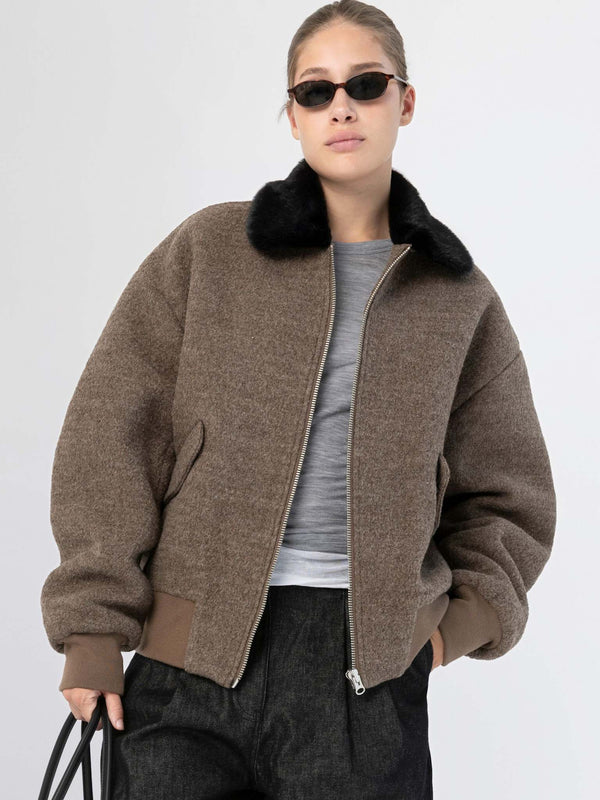 A model wears a stylish brown bomber jacket with a black fur collar, paired with a gray top and dark pants, showcasing MEOTINE's chic design.