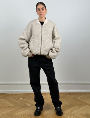 A model wears a cozy beige bomber jacket with a textured finish, paired with black pants and stylish shoes, showcasing MEOTINE's design.