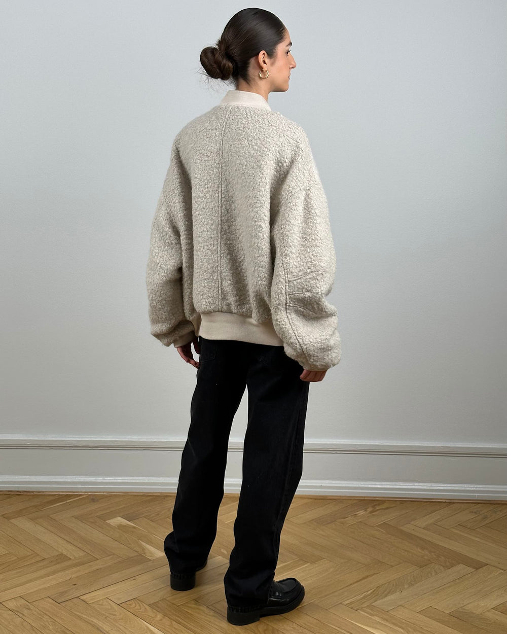 A model wears a cozy beige bomber jacket with a textured finish, paired with black pants and stylish shoes, showcasing MEOTINE's design.