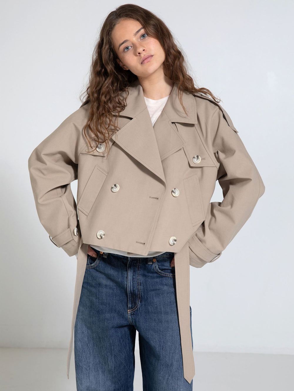 A model showcases a stylish beige cropped jacket with a double-breasted design and tie details, paired with loose jeans. MEOTINE.