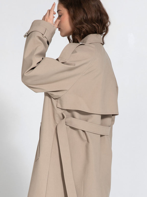 A side view of a woman wearing a stylish beige trench coat with a layered design, showcasing MEOTINE's elegant fashion.