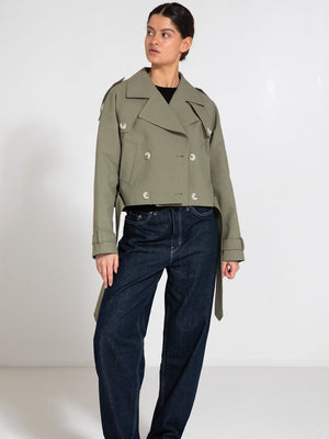Stylish cropped trench coat in olive green, featuring double-breasted buttons and a belted waist, paired with dark denim pants. MEOTINE.