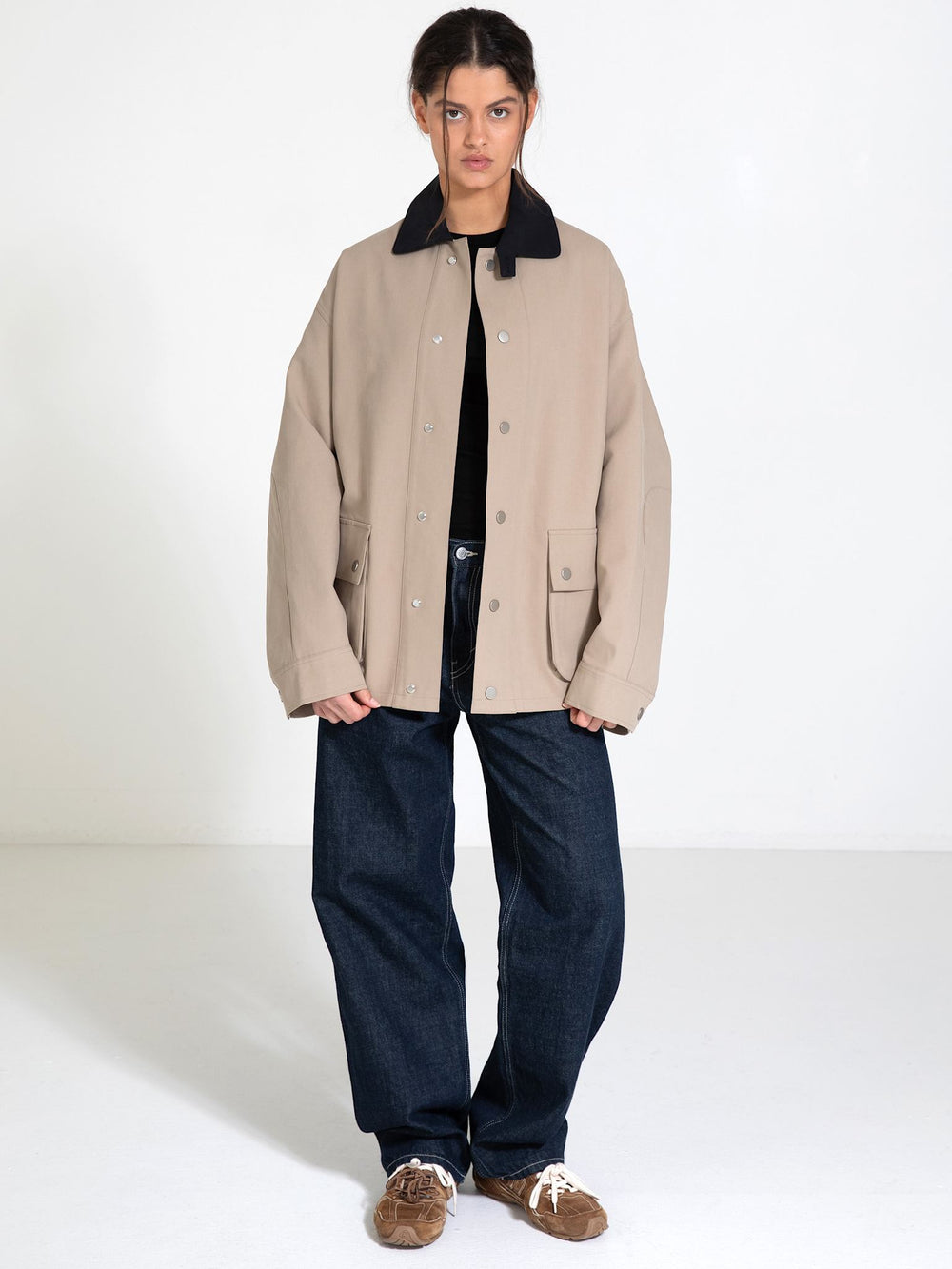 A model stands in a spacious room wearing a beige MEOTINE jacket with a black collar, paired with loose blue jeans and brown shoes.
