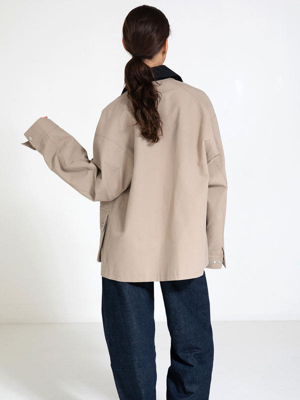 A woman in a beige oversized shirt with a black collar, styled with dark denim pants, showcasing a relaxed look by MEOTINE.