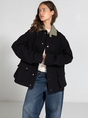 A model wears a black MEOTINE jacket with a green collar, paired with loose denim jeans, showcasing a casual, stylish look.
