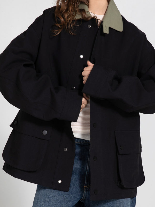 A model wears a stylish black MEOTINE jacket with a green collar, featuring large pockets and a relaxed fit, paired with jeans.