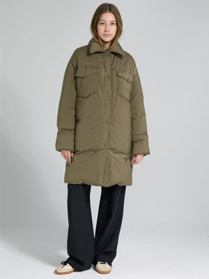 A model wears a long olive green puffer coat with a collar and front pockets, styled with black wide-leg pants. MEOTINE.