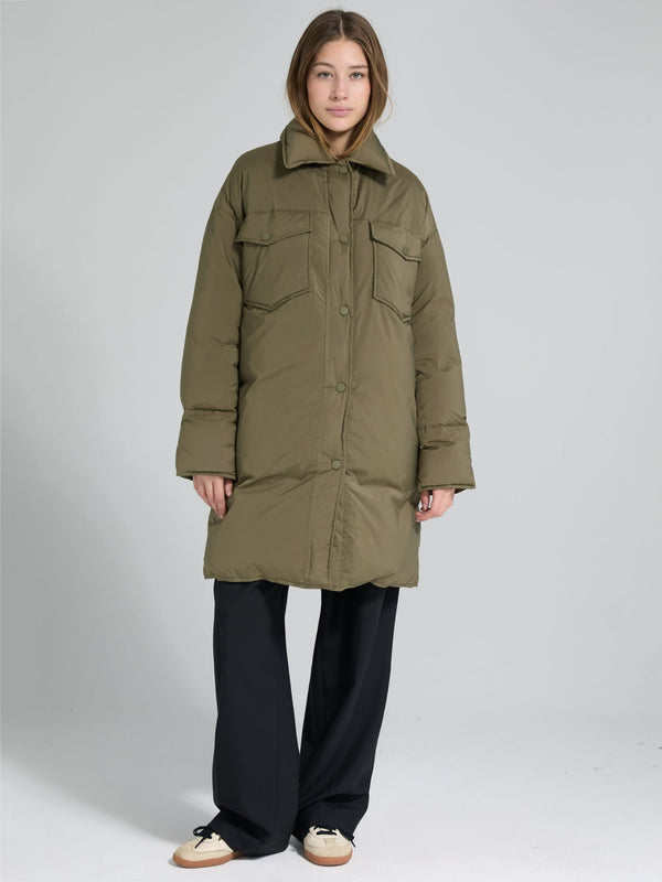 A model wears a long olive green puffer coat with a collar and front pockets, styled with black wide-leg pants. MEOTINE.