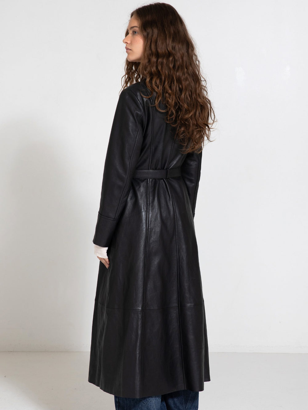 A model showcases a stylish black leather coat from MEOTINE, paired with a light top and wide-leg jeans, set against a plain background.