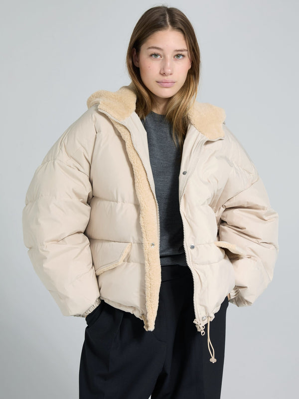 A model wears a cozy beige MEOTINE puffer jacket with a soft fur collar, paired with a gray top and black pants.