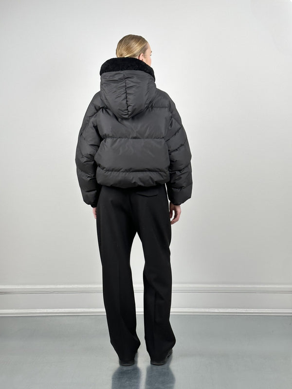 A model wearing a black puffer jacket with a hood, paired with black pants, showcasing a stylish winter look by MEOTINE.