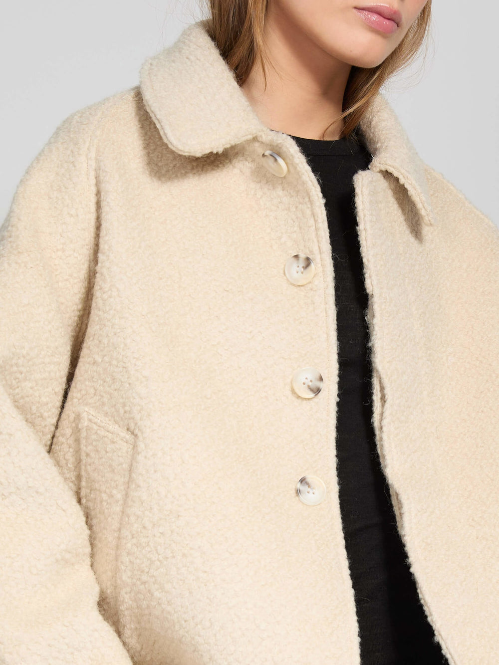 A model wears a cozy beige MEOTINE jacket with a button-up front, paired with a black top and blue jeans, exuding casual style.
