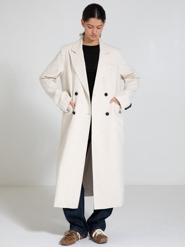 A model wears a stylish beige double-breasted coat by MEOTINE, paired with a black top and casual jeans, exuding modern elegance.