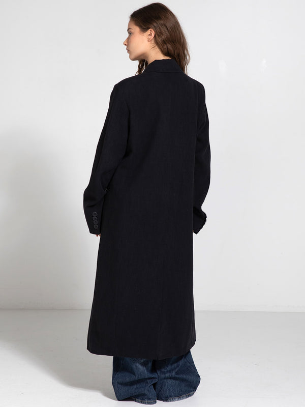A model showcases a long black coat with a relaxed fit, paired with wide-leg jeans, embodying MEOTINE's chic style.