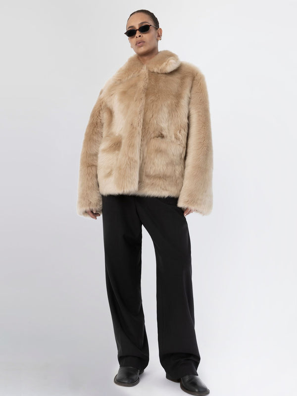 A model showcases a luxurious beige faux fur coat by MEOTINE, paired with sleek black trousers and stylish sunglasses.