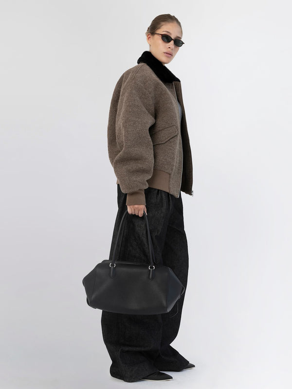 A model showcases a stylish brown bomber jacket with a black collar, paired with oversized black pants and sunglasses, holding a MEOTINE bag.