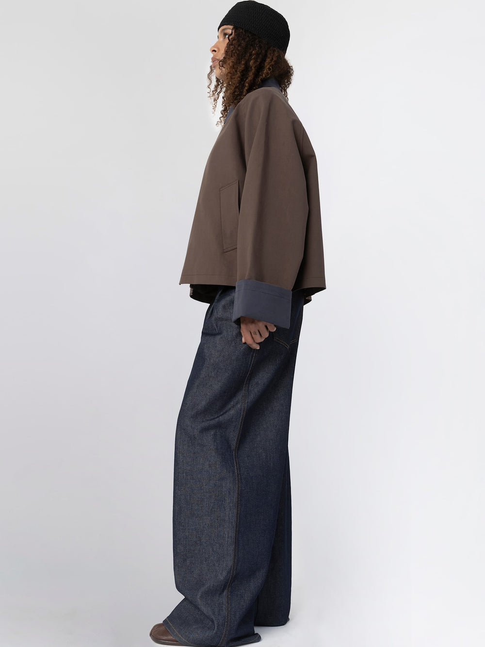 A model wears a brown MEOTINE jacket with a navy collar and cuffs, paired with dark denim pants and a black beanie.
