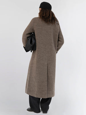 A model wearing a long brown coat with a relaxed fit, holding a black bag, showcasing MEOTINE's stylish design from the back.