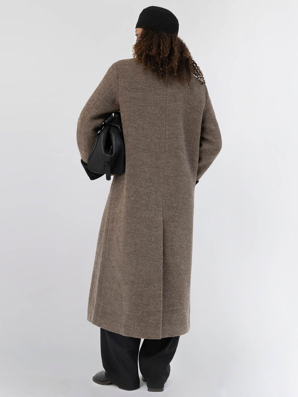 A model wearing a long brown coat with a relaxed fit, holding a black bag, showcasing MEOTINE's stylish design from the back.