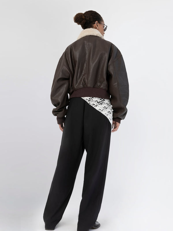 A model showcases a stylish brown leather bomber jacket with a cozy shearling collar, paired with loose black trousers. MEOTINE.