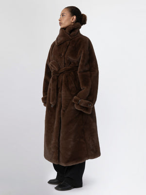 A model showcases a luxurious brown faux fur coat with a belted waist, featuring a high collar and a relaxed fit by MEOTINE.